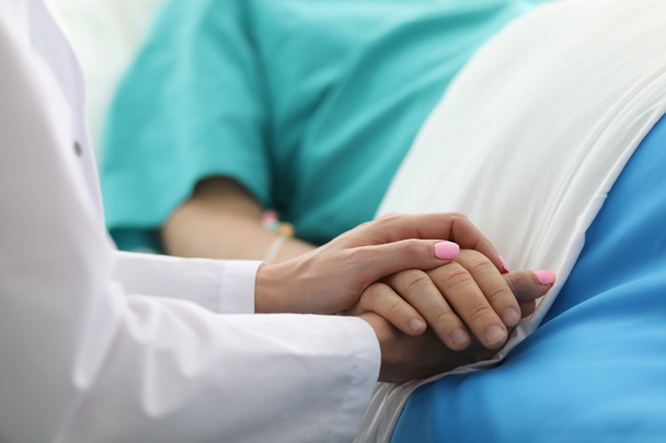 Vrouwelijke arts houdt zieke man ziekenhuisbed met de hand - Foto, afbeelding