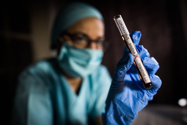 Fotografía conceptual de las manos de un médico sosteniendo y mirando un tubo de ensayo mientras con muestras positivas para la presencia de coronavirus (COVID-19
). - Foto, imagen
