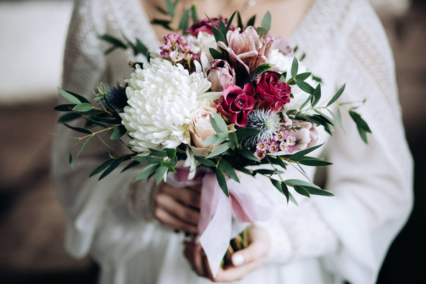 The bride holds a beautiful wedding bouquet of chrysanthemums and roses in rustic style - Photo, Image
