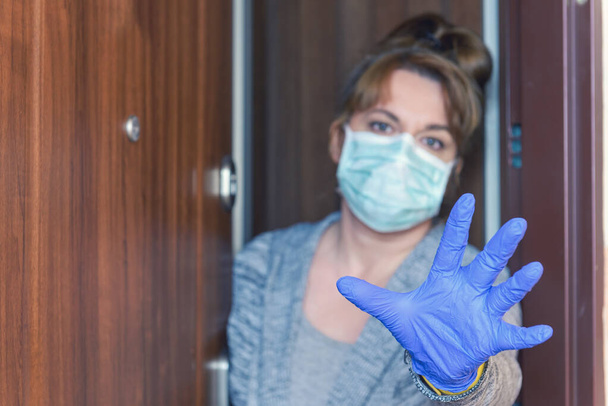 Korumalı yüz maskesi takan bir kadın Corona virüsü salgını yüzünden evinin kapılarını açıyor. Ev karantinası ve kendini izole etme kavramı - Fotoğraf, Görsel