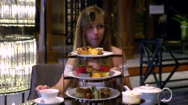 Gyönyörű fiatal nő eszik kis torták és ivóvíz tea a Luxury Restaurant - Felvétel, videó