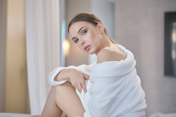 Beautiful young woman in bathrobe resting on bed after shower at home - Фото, зображення
