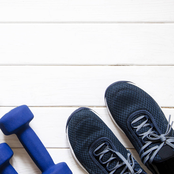 Sportfelszerelés. Kék női cipők, kék súlyzók és fehér mérlegek állnak fehér fa háttéren - Fotó, kép