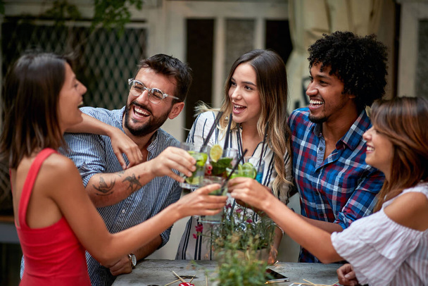 Cheerful friends taps with glasses and toasts with drink - Foto, afbeelding