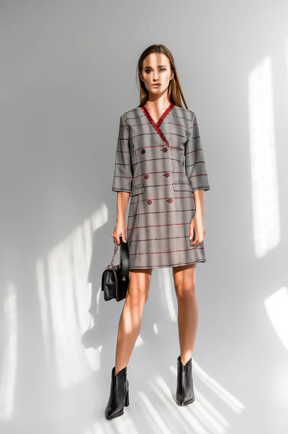 Attractive brown-haired woman in a gray checkered dress on a white background. Photosession for a clothing catalog - Fotoğraf, Görsel