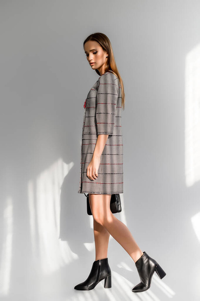 Attractive brown-haired woman in a gray checkered dress on a white background. Photosession for a clothing catalog - Φωτογραφία, εικόνα