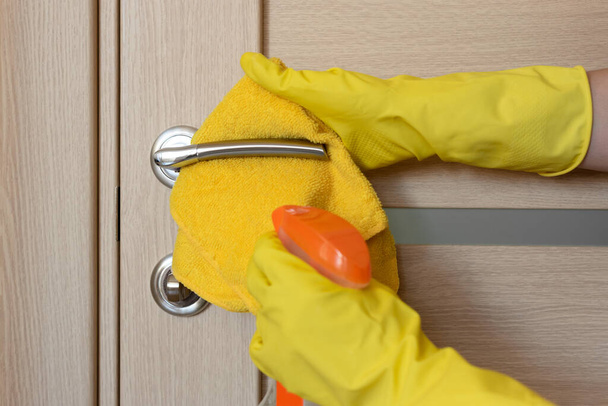 Female hand in rubber protective glove with rag wiping door handle using cleaning spray. - Fotografie, Obrázek