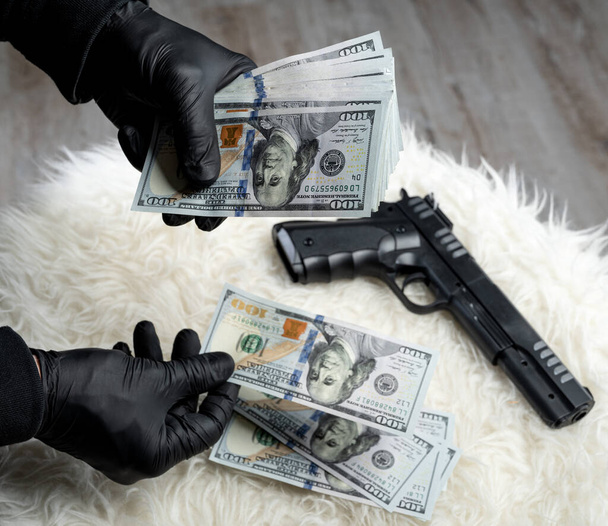 Close-up view of gun and dollars in hands of robber in gloves - Фото, изображение