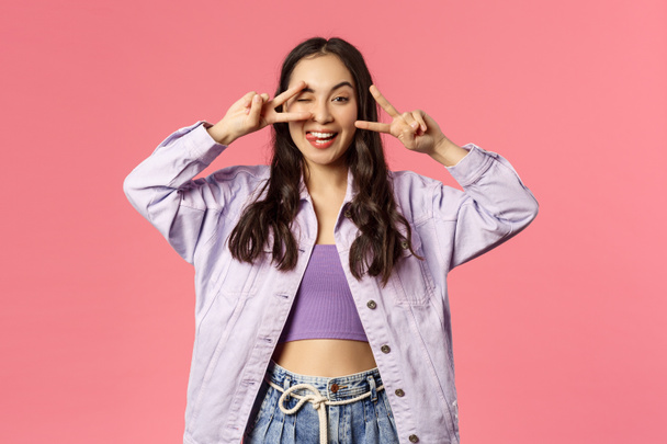 Love and peace people. Cheerful carefree attractive girl sending positivity and happiness, show goodwill kawaii sign and smiling, being in good mood, enjoying end of quarantine, pink background - Photo, image