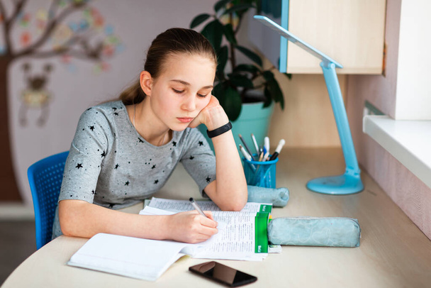 Beautiful young school girl working at home in her room with class notes and mobile phone and studying. Distance education and learning concept during quarantine - Фото, зображення