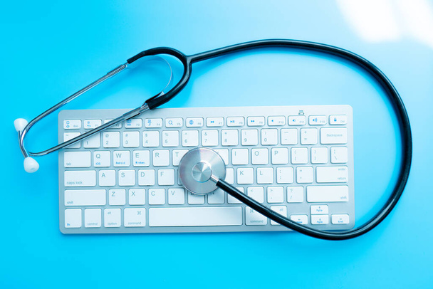 Sağlık ve ilaç veya bilgisayar antivirüs koruması ve onarım hizmeti konsepti: iş yeri bilgisayarındaki seçici odak efektli dizüstü bilgisayar klavyesinde mavi steteskopun makro görünümü - Fotoğraf, Görsel