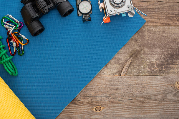 ylhäältä näkymä carabiners, vaellus köysi, kiikarit, kompassi ja kaasupoltin sininen nukkuva matto puupinnalla
 - Valokuva, kuva