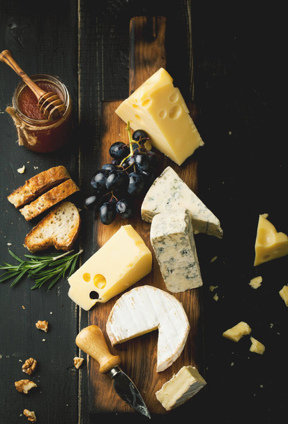 Assorted cheeses with grapes, nuts and rosemary on a wooden background - Foto, Bild