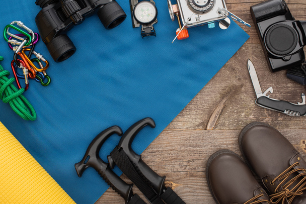 Draufsicht auf Wanderausrüstung auf blauer Isomatte, Fotokamera und Stiefeln auf Holztisch - Foto, Bild