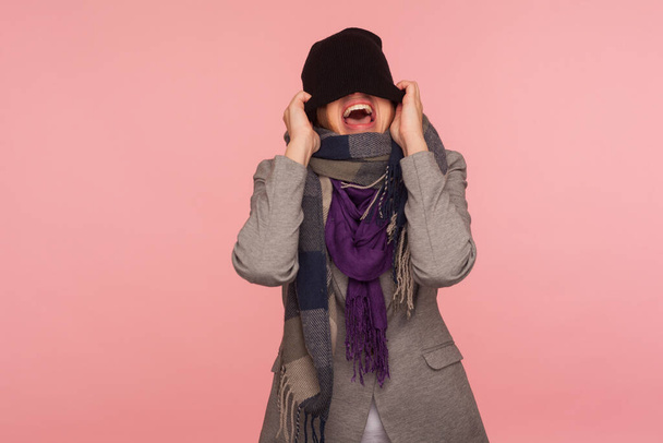 Portrait of angry mad girl in scarf pulling hat over her eyes and shouting, feeling crazy pissed off and desperate, autumn depression, nervous break down. studio shot isolated on pink background - Фото, изображение