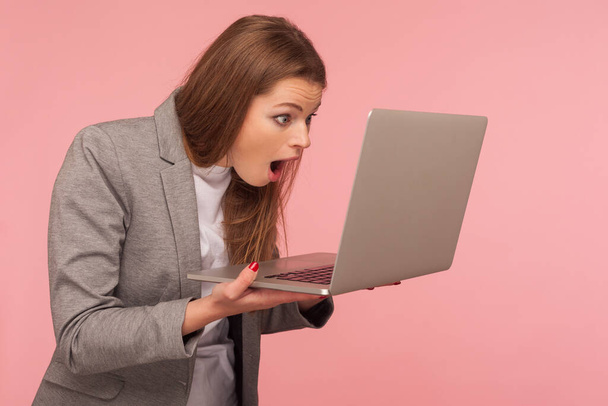 Portrait of amazed young businesswoman looking at laptop with open mouth, surprised expression, having problems with computer, software failure, error. indoor studio shot isolated on pink background - Photo, image