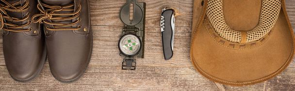 panoramic shot of boots, compass, jackknife and hat on wooden table - Foto, Bild