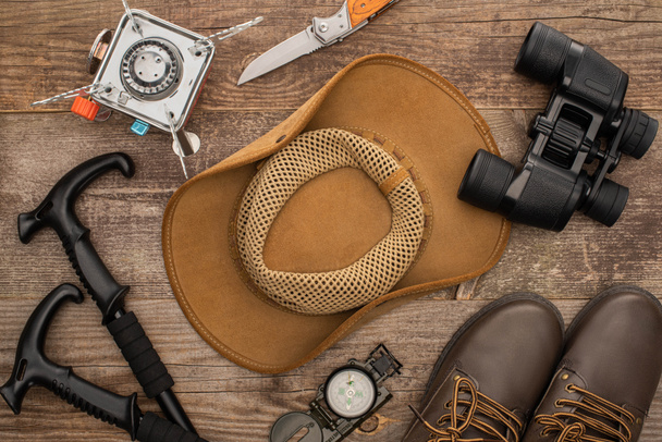 bovenaanzicht van hoed, laarzen, wandelstokken, verrekijker, jaknife en gasbrander op houten ondergrond - Foto, afbeelding