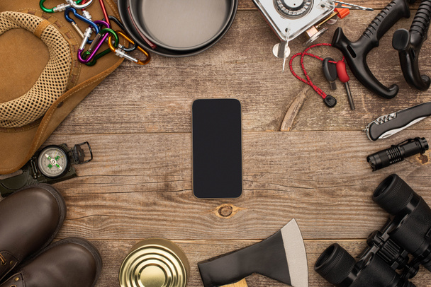 vista superior del smartphone con pantalla negra cerca del equipo de senderismo en la mesa de madera
 - Foto, Imagen