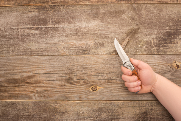 partial view of man holding jackknife on wooden table - Fotografie, Obrázek