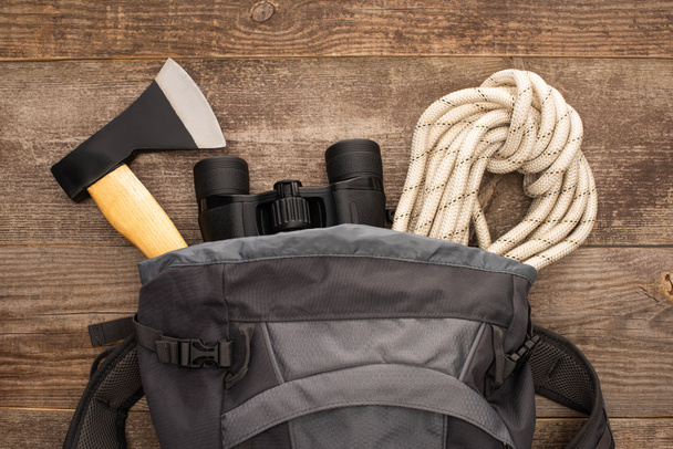 top view of backpack with axe, hiking rope and binoculars on wooden surface - Photo, Image