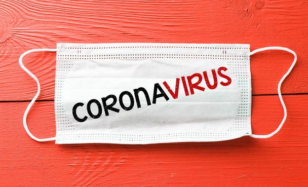 КОРОНАВИРУС. Слово написано на защитной маске, расположенной на красном столе. Новый коронавирус - 2019-nCoV, концепция вируса WUHAN
 - Фото, изображение
