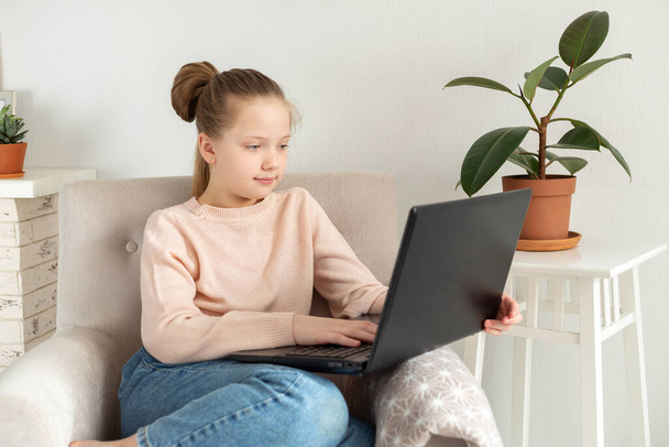Schoolgirl using laptop computer on armchair. Home school, online education, home education, quarantine concept - Image - 写真・画像