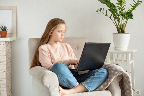 Schoolgirl using laptop computer on armchair. Home school, online education, home education, quarantine concept - Image - Fotó, kép