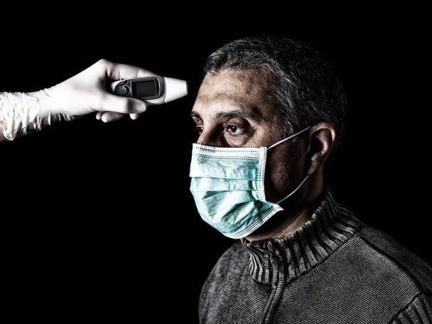 mies, jonka kuume mitataan tai otetaan digitaalisen lämpömittarin avulla sairaanhoitajan toimesta. Pandemia tai epidemia, pelottava, pelko tai vaara käsite. Biologisen vaaran, kuten COVID-19 alias koronaviruksen, torjunta
.  - Valokuva, kuva