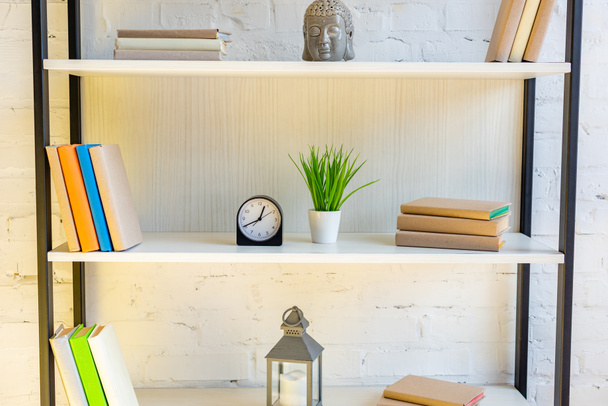 estantes con libros, reloj, planta de la casa, linterna y cabeza de buda
 - Foto, Imagen