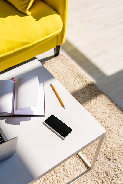 obývací pokoj s pohovkou a stolem s laptopem, smartphonem a poznámkovým blokem na slunci - Fotografie, Obrázek