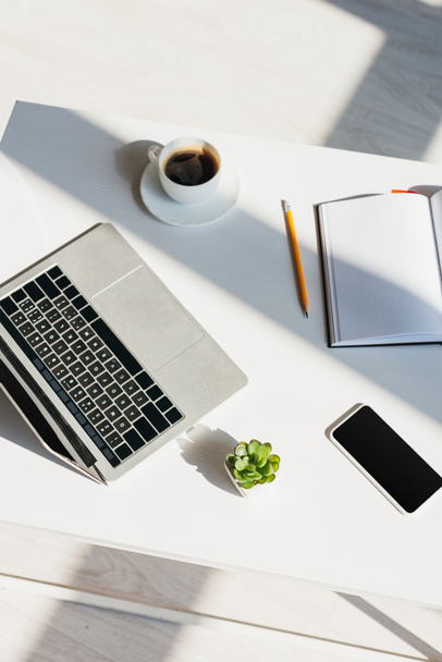 munkahelyi laptop, okostelefon, jegyzettömb és kávéscsésze napfényben - Fotó, kép