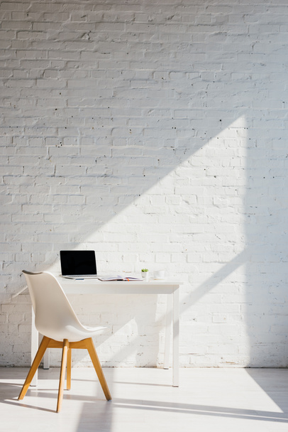 Home Office mit Laptop auf Tisch und Stuhl in der Nähe im Sonnenlicht - Foto, Bild