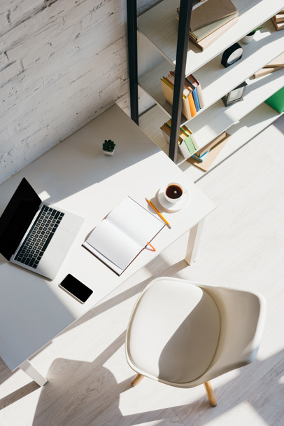ylhäältä näkymä kotitoimistoon kannettavalla tietokoneella, älypuhelimella ja kupillisella kahvia auringonvalossa
 - Valokuva, kuva