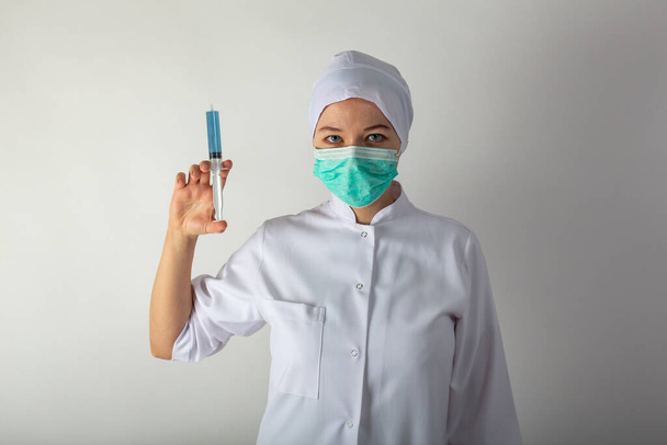 Tıp önlüklü kız elinde mavi sıvı Coronaviris aşısı olan büyük bir şırınga tutuyor. - Fotoğraf, Görsel