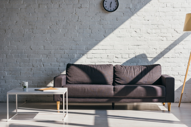 sala de estar con sofá gris y mesa con taza de café, bloc de notas y suculenta a la luz del sol
 - Foto, imagen