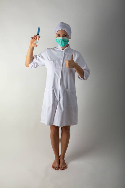 Meisje in een medische jas heeft een grote spuit met blauwe vloeistof - coronavirisvaccin - Foto, afbeelding