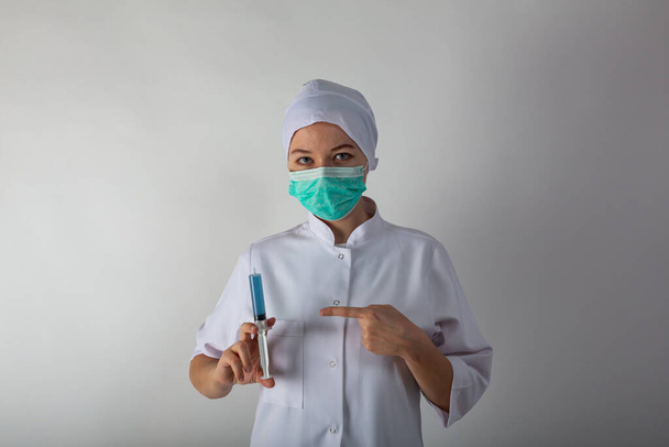 Κορίτσι σε ένα ιατρικό παλτό κρατά μια μεγάλη σύριγγα με μπλε υγρό - εμβόλιο coronaviris - Φωτογραφία, εικόνα