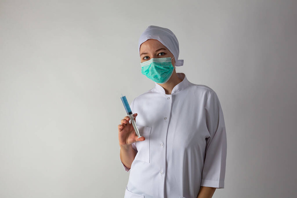 Niña con una capa médica sostiene una jeringa grande con líquido azul - vacuna coronaviris
 - Foto, Imagen
