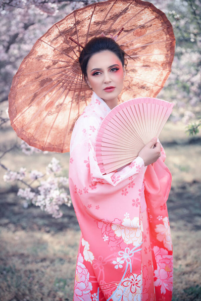 春の果樹園で日本の伝統的な着物と傘を身に着けている美しい女の子 - 写真・画像