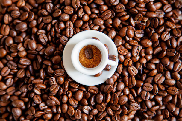 Kahve çekirdeğinin üzerinde küçük beyaz bir fincan kahve duruyor. Üst görünüm. - Fotoğraf, Görsel