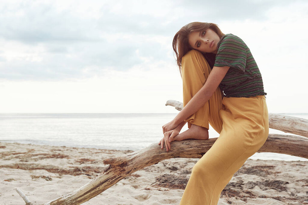 όμορφη μοντέρνα κοπέλα στην παραλία ντυμένη με πράσινη μπλούζα και κίτρινο παντελόνι, μοντέρνα ρετρό ρούχα, τρόπο ζωής και μόδας - Φωτογραφία, εικόνα