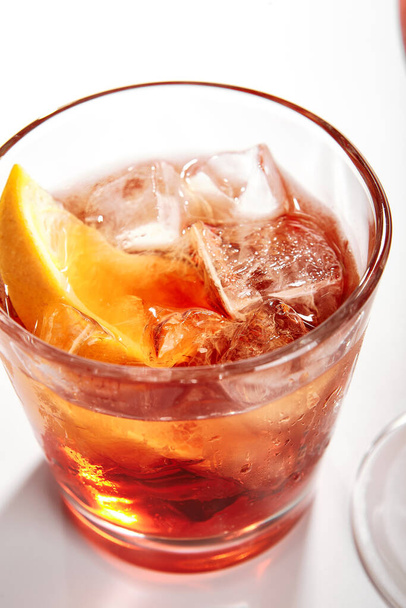 Negroni koktél közelről. Alkohol erős aperitif ital üveg oldalnézetben. Piros vermutos ital, Campari likőr, gin, narancs és jég az italokban. Olasz koktéladag üvegedényekben - Fotó, kép