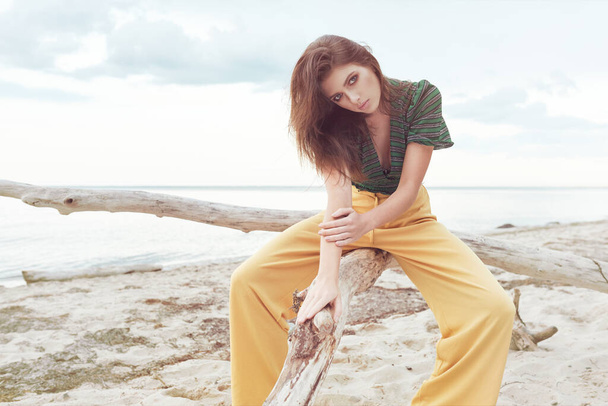beautiful fashionable girl on the beach dressed in a green sweatshirt and yellow pants, stylish retro clothing, lifestyle and fashion - Photo, Image