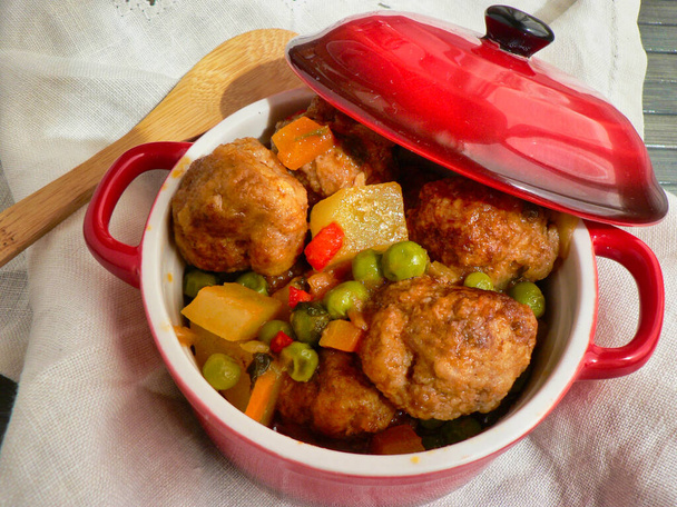 Boulettes de viande avec pommes de terre et pois dans une casserole rouge, cuillère en bois et nappe blanche
 - Photo, image