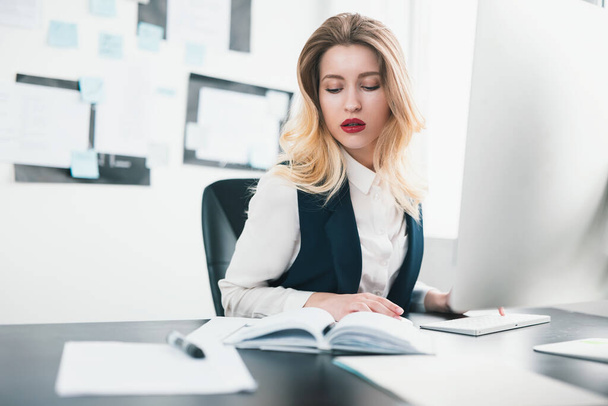 молодая блондинка красивая женщина-менеджер работает в своем современном офисе, проверяя ее расписание встреч в ее планировщик, многозадачность, концепция работы
. - Фото, изображение