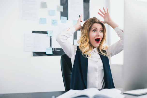 young blond beautiful woman manager works in her modern office, holding her arms up in winning position after successful negotiations, looks amazed multitasking, work concept. - Photo, Image