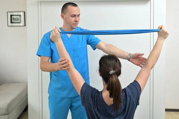 Ein junger männlicher Physiotherapeut hilft einem Teenie-Mädchen mit Dehnübungen  - Foto, Bild