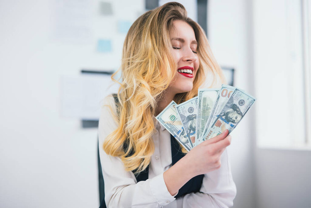 young blond sexy woman manager celebrating successful deal in the end of working day, holding cash like card deck in both hands, welfare concept. - Φωτογραφία, εικόνα