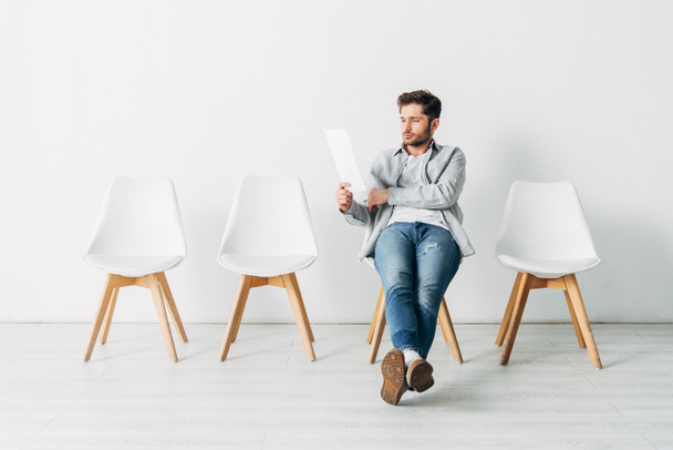 Handsome man looking at resume while sitting on chair in office - Foto, Imagem